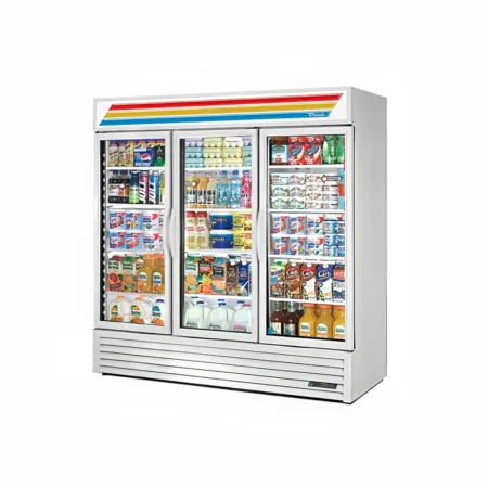A three-quarter perspective view of a large white True GDM-72 commercial refrigerator with three swing-out glass doors, fully stocked with various grocery items including eggs, yogurt, juice, and milk cartons.