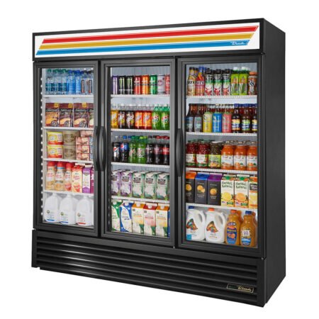 A three-quarter perspective view of a large black True GDM-72 commercial refrigerator featuring three swing-out glass doors, fully stocked with a wide variety of bottled water, soda, juices, milk cartons, and snacks.