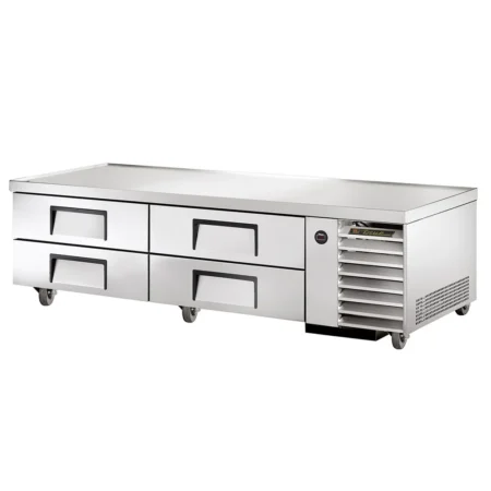 A perspective view of a stainless steel True commercial chef base featuring four refrigerated drawers with recessed handles, a heavy-duty flat top, and a side-mounted ventilation grille, all set on swivel casters.