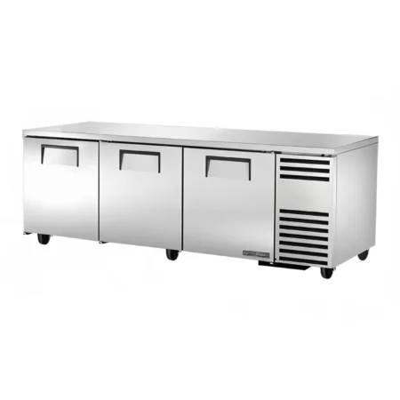 A Three-Quarter Perspective View Of A True Tuc-93 Stainless Steel Undercounter Refrigerator Featuring Three Solid Doors With Recessed Handles And A Side-Mounted Compressor Compartment.